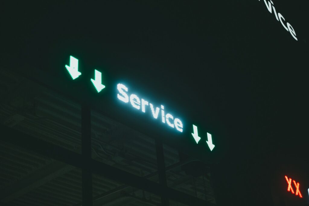 Glowing teal digital neon sign displaying the word "Service" flanked by downward arrow symbols in a dark setting.