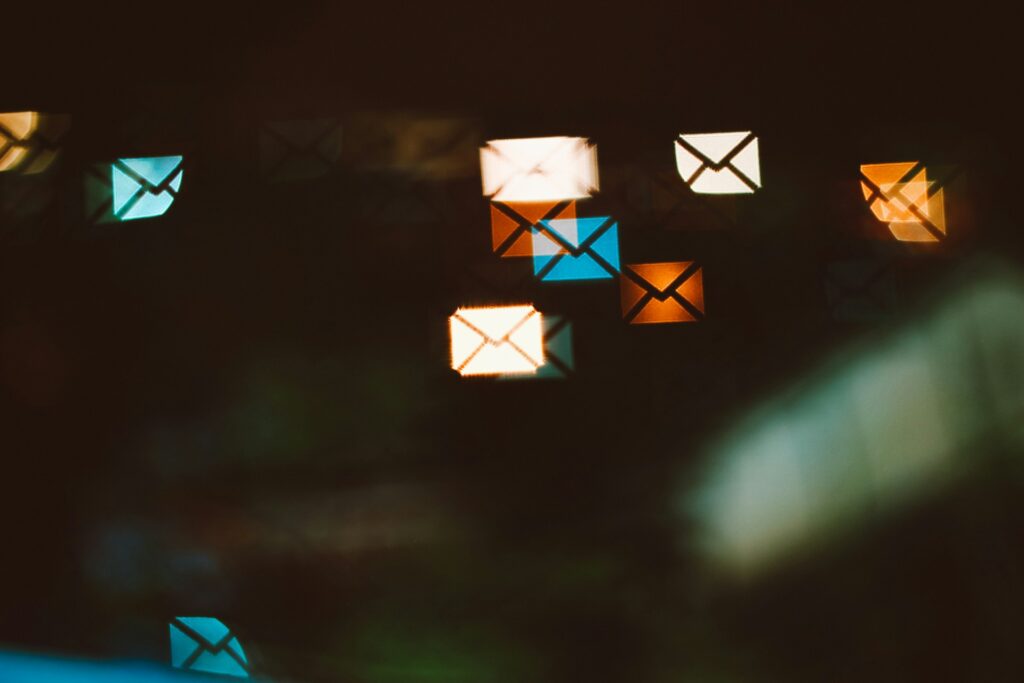 Colorful bokeh light shapes of glowing envelope icons floating against a dark background representing digital communication and email marketing strategy.
