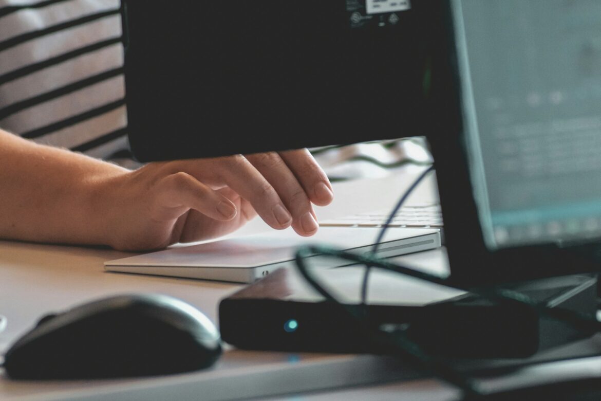 Close-up of a digital marketer's hand using a trackpad and computer setup while analyzing SEO performance and optimization data.